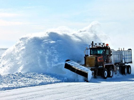 A very large industrial plow clearing several feet of snow from a highway.