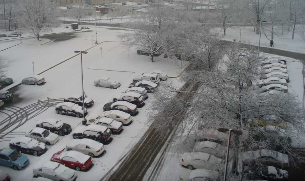 A parking lot with cars is shown in Syracuse NY as snow piles up.